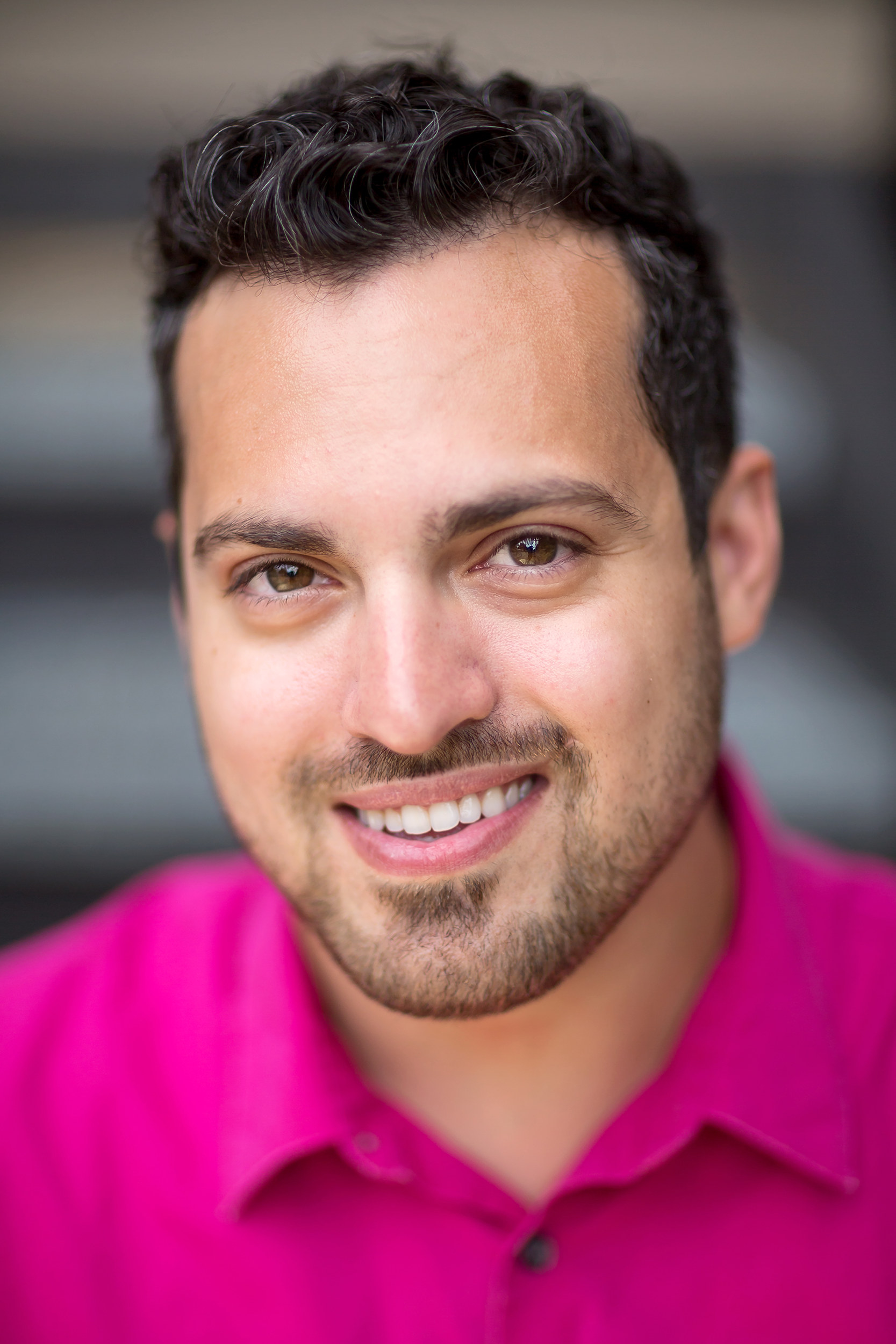 Handsome man in a pink shirt smiling.