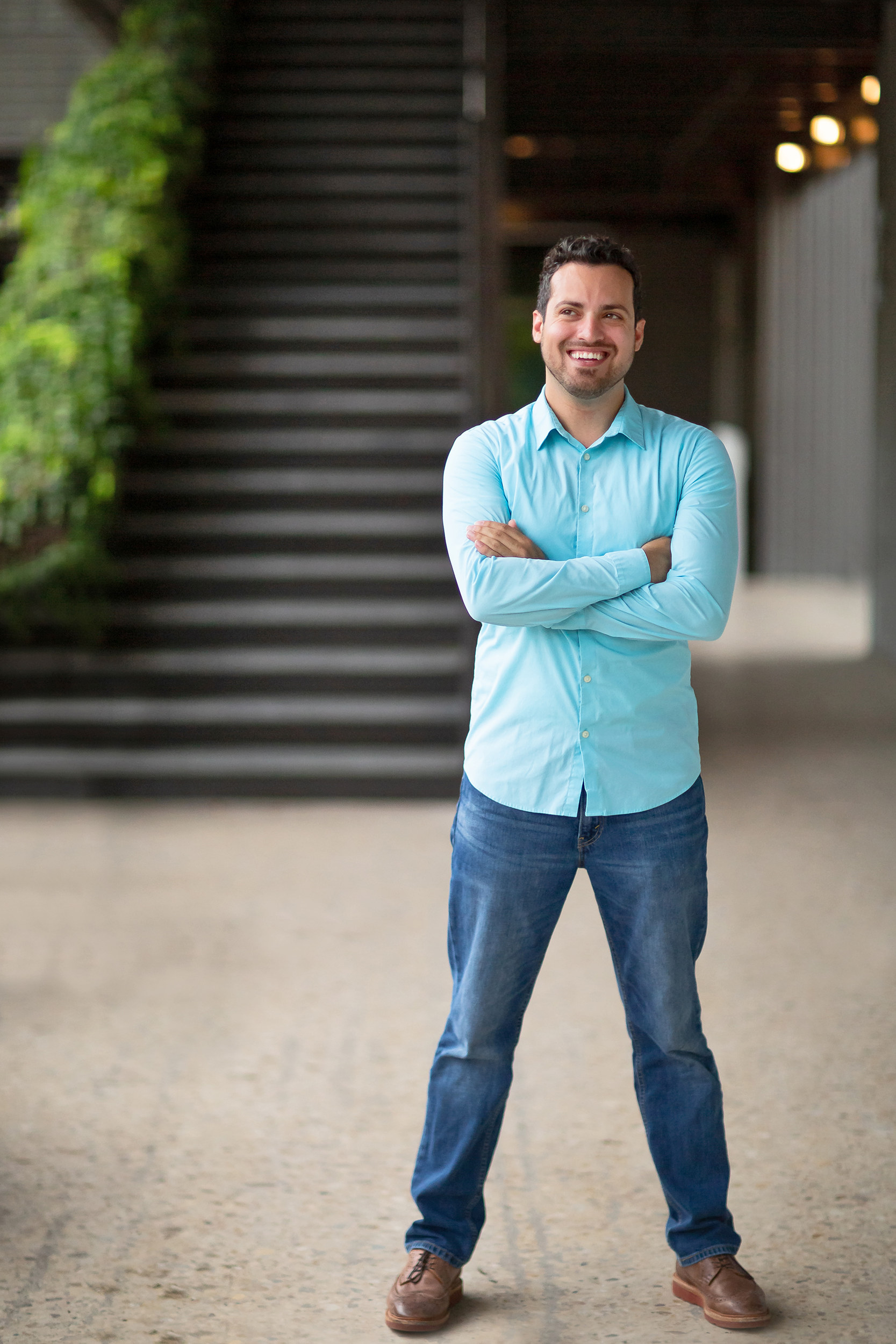 Handsome man in a light blue shirt and jeans standing in front of a staircase.